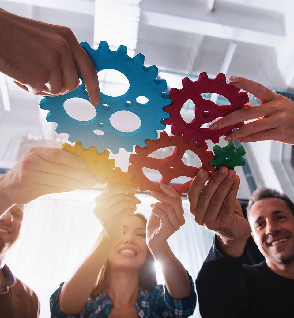 Flera personer håller ihop färgade kugghjul med händerna, som visuellt illustrerar hur olika delar samverkar.